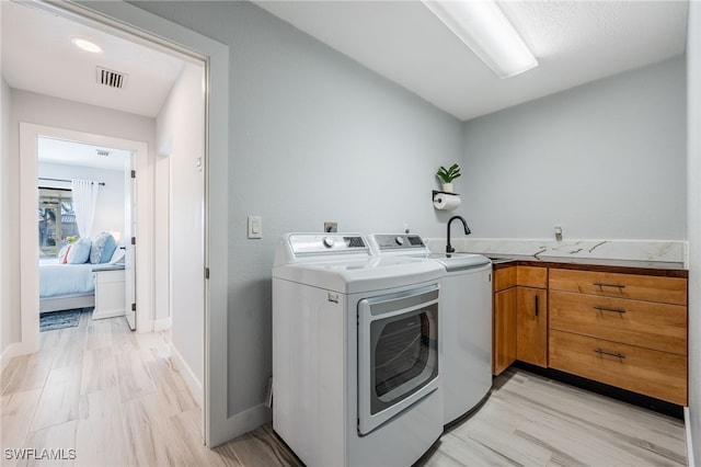 laundry room featuring cabinets, sink, washing machine and dryer, and light wood-type flooring