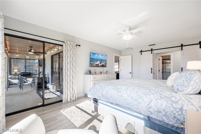 bedroom with access to exterior, a barn door, ceiling fan, and light wood-type flooring