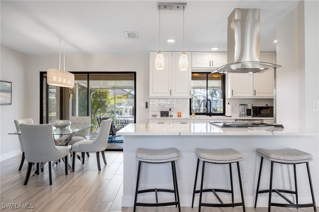 kitchen with white cabinetry, decorative light fixtures, island range hood, and decorative backsplash