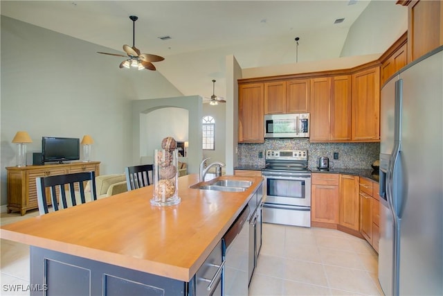 kitchen with sink, a kitchen island with sink, backsplash, stainless steel appliances, and light tile patterned flooring