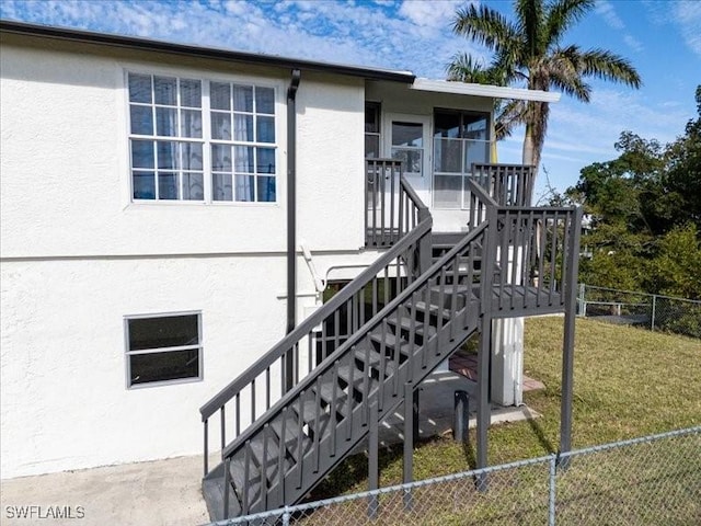 exterior space featuring stairs, a yard, fence, and stucco siding