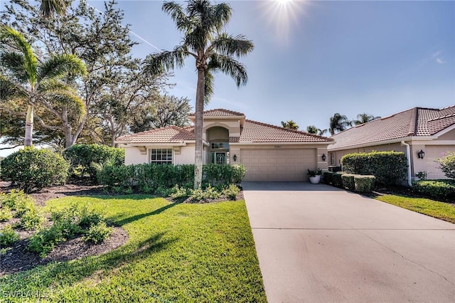 mediterranean / spanish house featuring an attached garage, a tile roof, driveway, stucco siding, and a front lawn