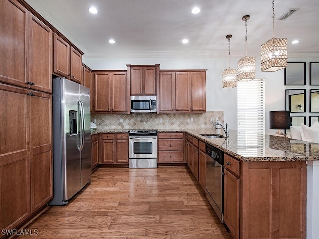 kitchen with appliances with stainless steel finishes, decorative light fixtures, sink, light stone counters, and kitchen peninsula