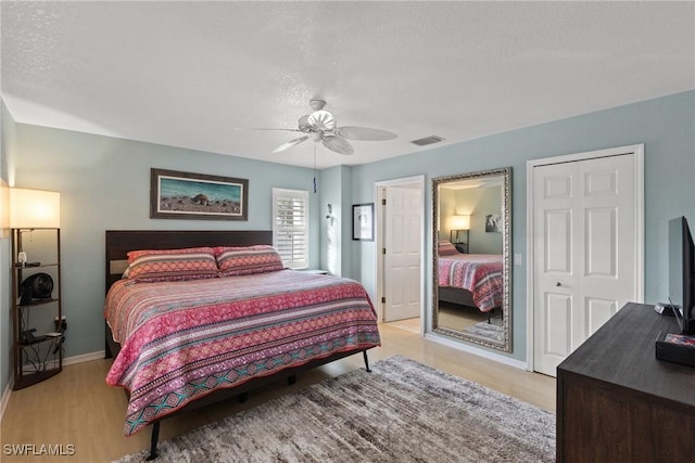 bedroom with visible vents, baseboards, light wood-style flooring, ceiling fan, and a textured ceiling