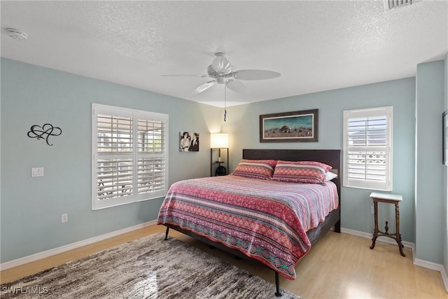 bedroom with light wood-style flooring, baseboards, ceiling fan, and a textured ceiling