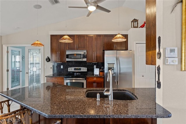 kitchen featuring appliances with stainless steel finishes, dark stone counters, a sink, and decorative light fixtures