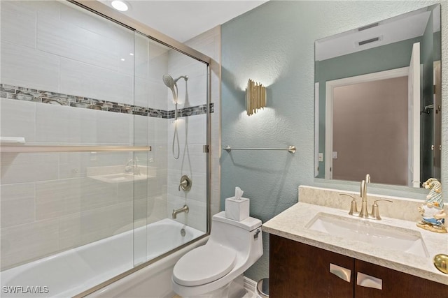 full bathroom with a textured wall, shower / bath combination with glass door, vanity, and toilet