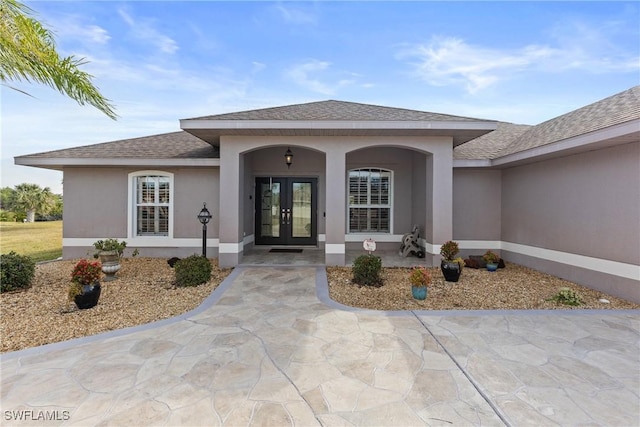 doorway to property featuring french doors, roof with shingles, and stucco siding