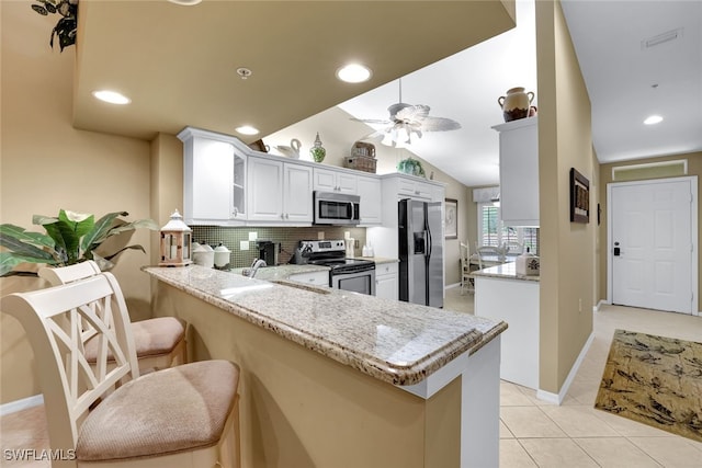 kitchen featuring white cabinetry, appliances with stainless steel finishes, kitchen peninsula, and light stone counters