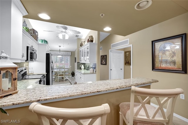 kitchen with a breakfast bar area, appliances with stainless steel finishes, white cabinets, vaulted ceiling, and kitchen peninsula