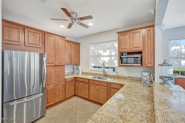 kitchen with light tile patterned flooring, appliances with stainless steel finishes, sink, ceiling fan, and light stone counters