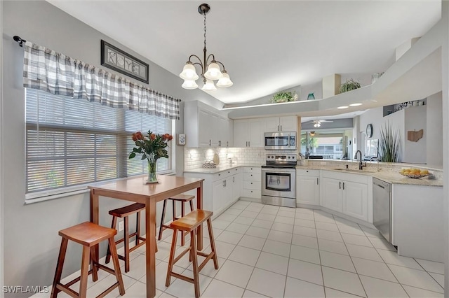 kitchen with white cabinetry, vaulted ceiling, pendant lighting, stainless steel appliances, and decorative backsplash