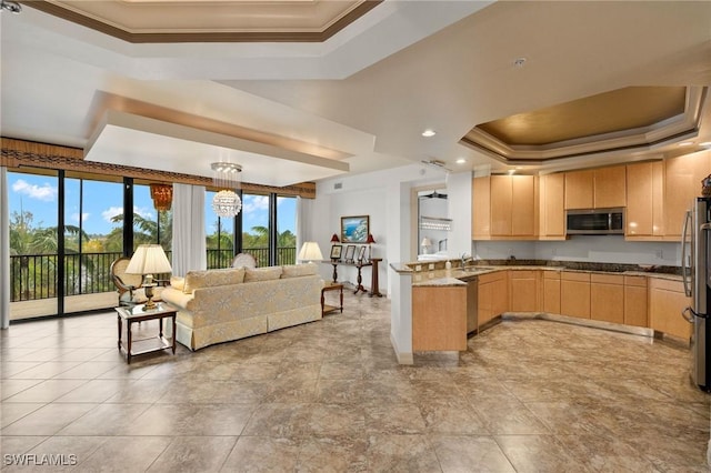 kitchen featuring ornamental molding, appliances with stainless steel finishes, light brown cabinets, and a tray ceiling