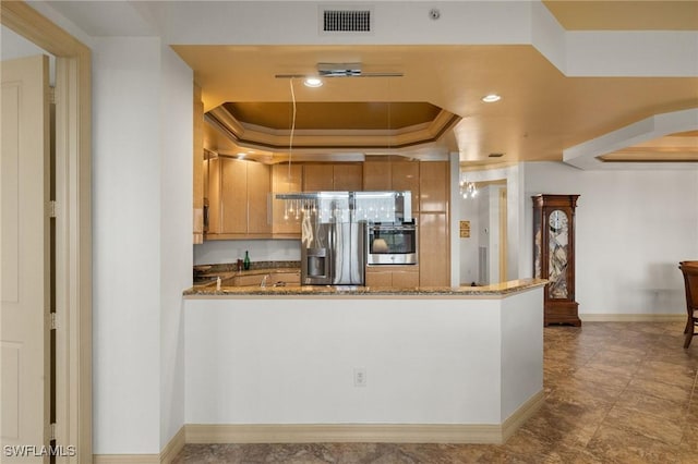 kitchen with crown molding, appliances with stainless steel finishes, a tray ceiling, kitchen peninsula, and stone counters