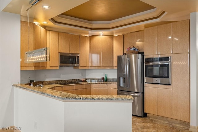 kitchen with a peninsula, light stone countertops, appliances with stainless steel finishes, and a tray ceiling