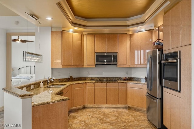 kitchen featuring sink, appliances with stainless steel finishes, a tray ceiling, light stone countertops, and kitchen peninsula