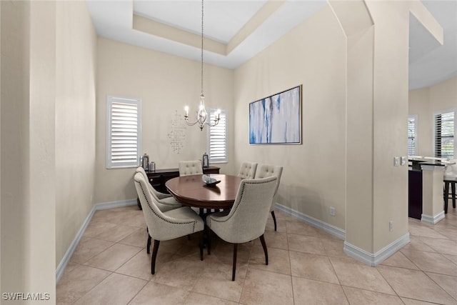 dining area featuring light tile patterned flooring, a healthy amount of sunlight, a chandelier, and a tray ceiling