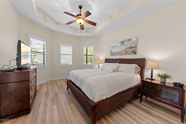 bedroom with ceiling fan, a tray ceiling, and light hardwood / wood-style floors