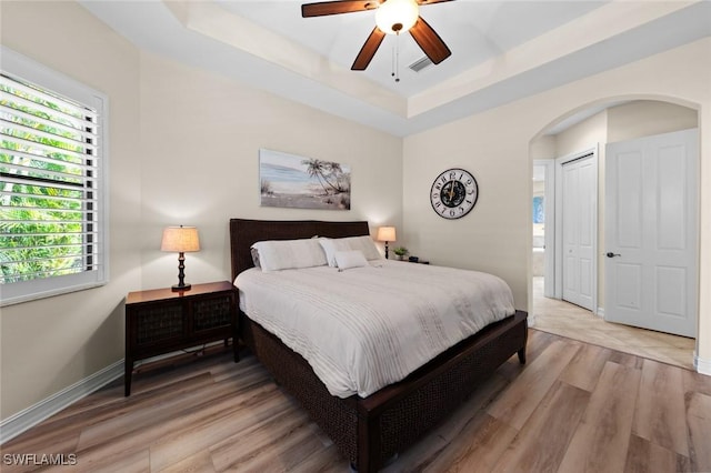 bedroom featuring ceiling fan, a raised ceiling, a closet, and light hardwood / wood-style flooring