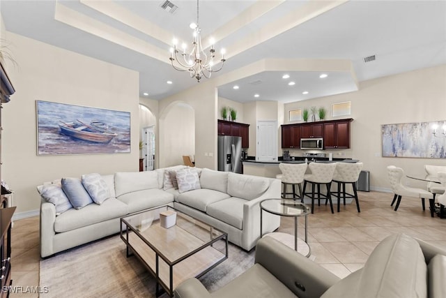 living room with a notable chandelier, a raised ceiling, and light tile patterned flooring