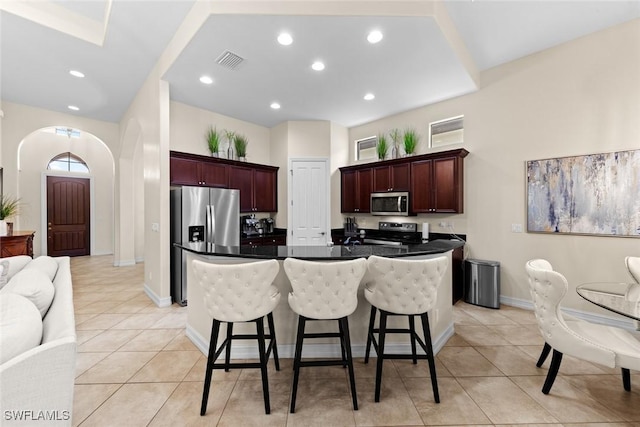 kitchen with a center island with sink, appliances with stainless steel finishes, a breakfast bar area, and light tile patterned floors