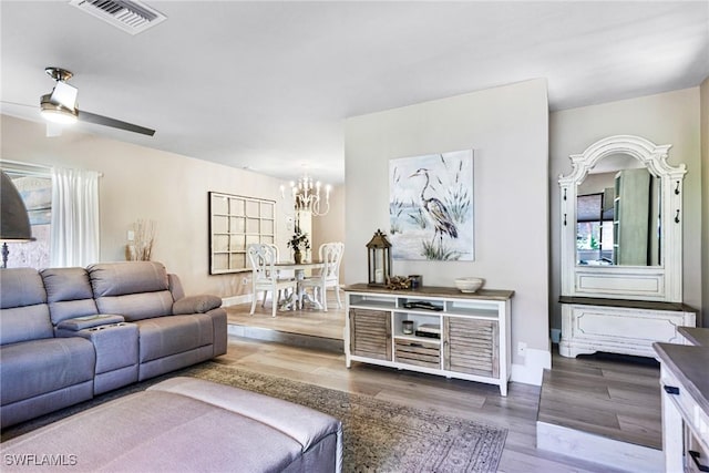 living area featuring visible vents, plenty of natural light, ceiling fan with notable chandelier, and wood finished floors