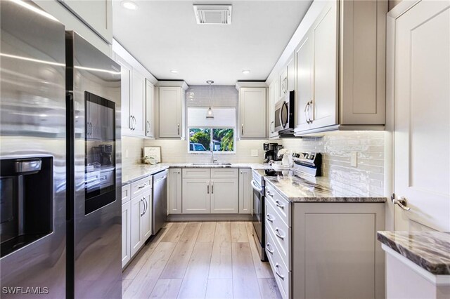 kitchen with stone countertops, decorative light fixtures, sink, stainless steel appliances, and light hardwood / wood-style flooring