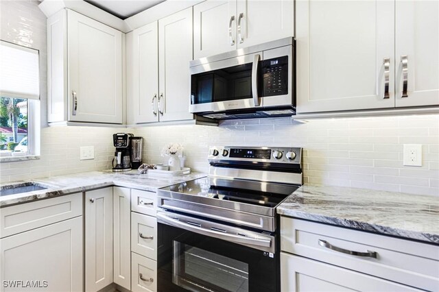 kitchen with tasteful backsplash, light stone counters, white cabinets, and appliances with stainless steel finishes