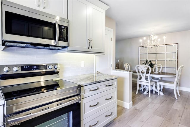 kitchen featuring stainless steel appliances, white cabinets, light wood-type flooring, backsplash, and a chandelier