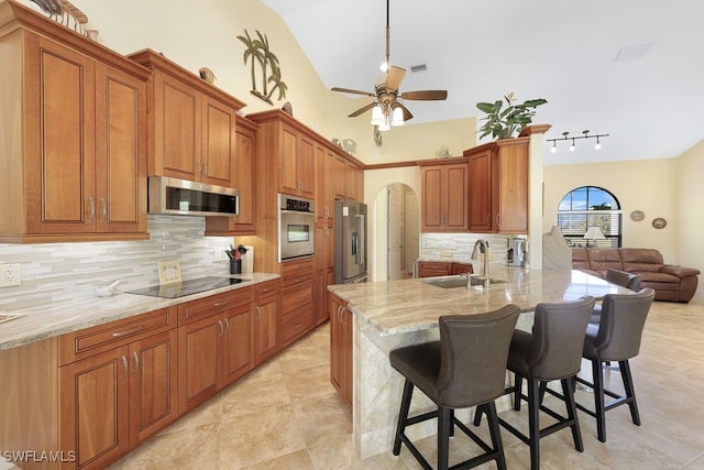 kitchen featuring stainless steel appliances, light stone countertops, sink, tasteful backsplash, and a breakfast bar area