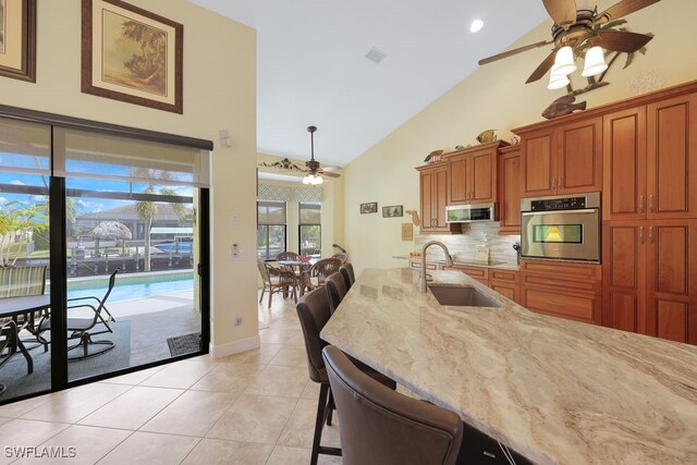 kitchen featuring stainless steel appliances, light tile patterned flooring, backsplash, sink, and a kitchen bar