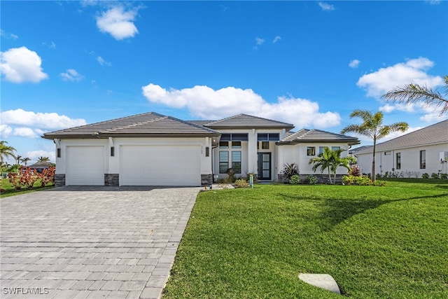 prairie-style home featuring an attached garage, stone siding, decorative driveway, stucco siding, and a front lawn