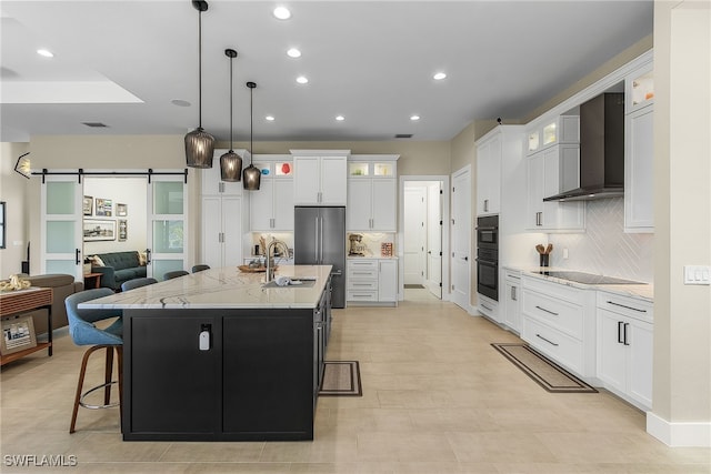 kitchen featuring a barn door, a sink, a kitchen breakfast bar, wall chimney range hood, and black appliances