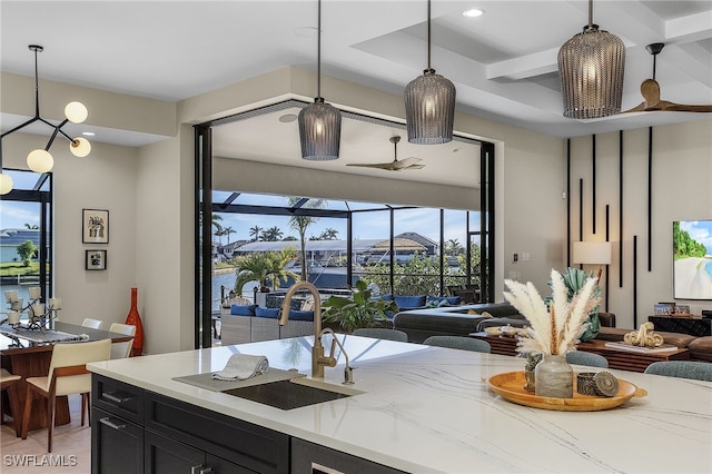 kitchen featuring light stone counters, decorative light fixtures, open floor plan, a sink, and dark cabinetry