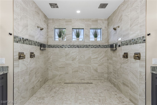 bathroom featuring a healthy amount of sunlight, tiled shower, and vanity