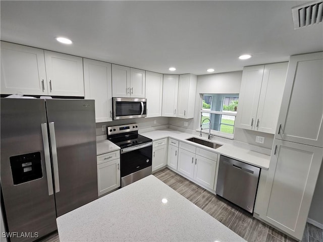 kitchen with sink, white cabinetry, stainless steel appliances, light stone counters, and dark hardwood / wood-style flooring