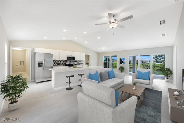 living room with vaulted ceiling, ceiling fan, and light wood-type flooring