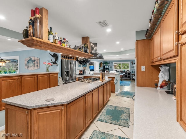 kitchen featuring wall chimney range hood, appliances with stainless steel finishes, light tile patterned floors, and kitchen peninsula