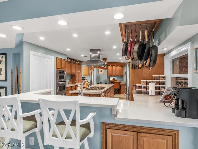 kitchen with sink, a breakfast bar area, stainless steel appliances, island range hood, and kitchen peninsula