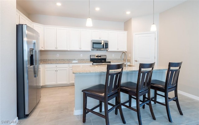 kitchen with decorative light fixtures, stainless steel appliances, white cabinets, and a kitchen bar