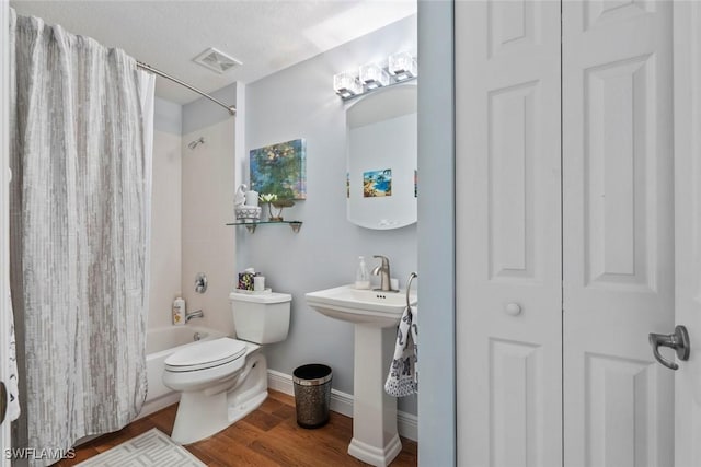 full bathroom with toilet, sink, a textured ceiling, hardwood / wood-style flooring, and shower / bath combination with curtain