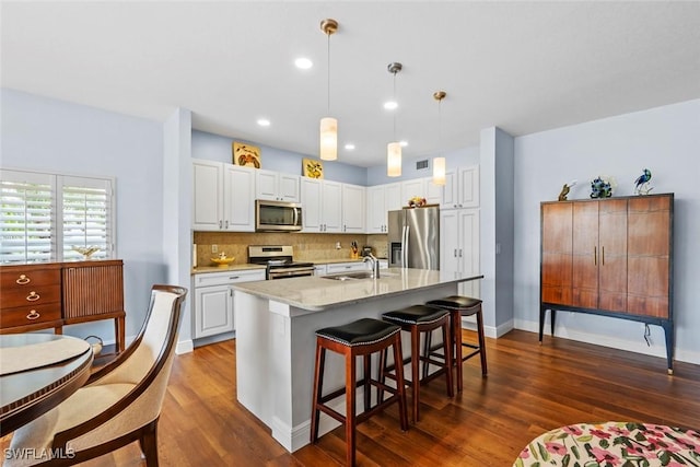 kitchen with an island with sink, sink, white cabinets, hanging light fixtures, and stainless steel appliances