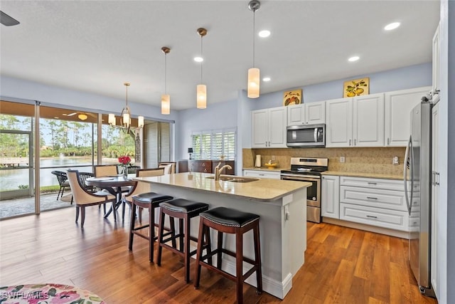 kitchen with stainless steel appliances, sink, white cabinets, and decorative light fixtures