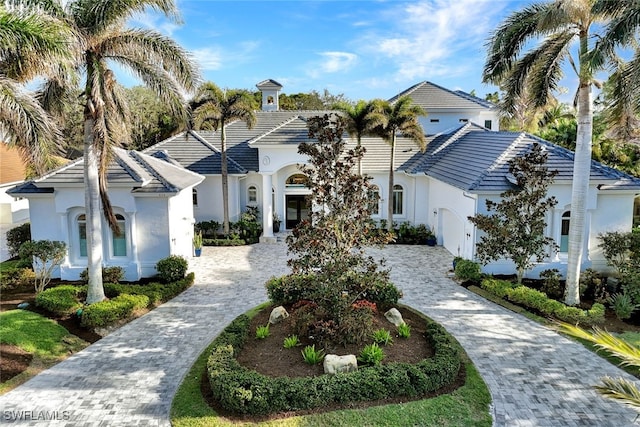 mediterranean / spanish house featuring a tiled roof, decorative driveway, and stucco siding