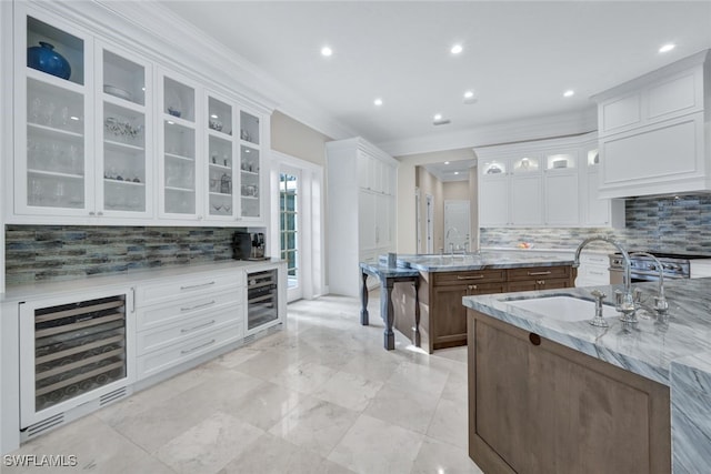 kitchen featuring sink, white cabinetry, light stone counters, an island with sink, and beverage cooler