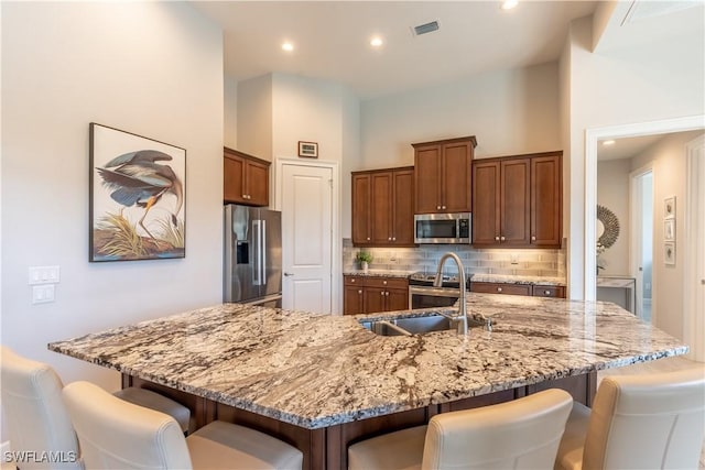 kitchen with stainless steel appliances, a towering ceiling, a breakfast bar area, and a large island with sink