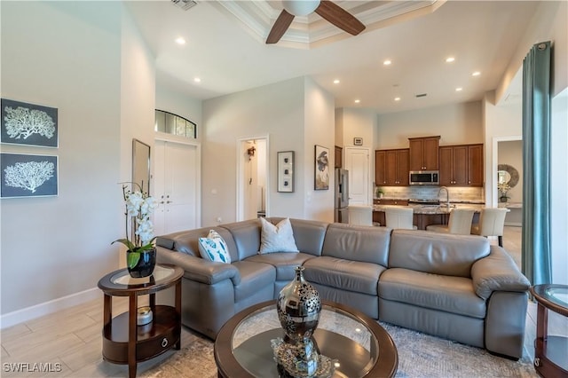 living room featuring sink, ornamental molding, a raised ceiling, ceiling fan, and a high ceiling