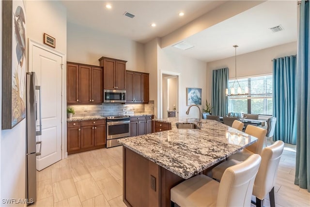 kitchen featuring pendant lighting, sink, stainless steel appliances, light stone countertops, and an island with sink