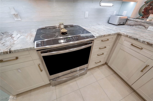 kitchen with cream cabinets, backsplash, light tile patterned floors, light stone countertops, and stainless steel electric range