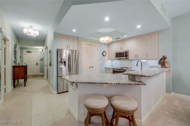 kitchen featuring a kitchen bar, light stone countertops, kitchen peninsula, and appliances with stainless steel finishes